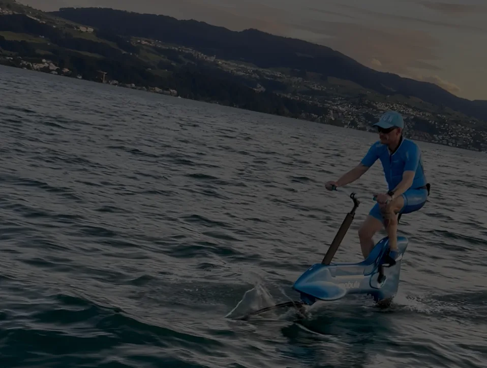 Cyrille C. Catel riding the Mobula bike foil across Lake Zurich at golden hour, the city shoreline and hills behind him.